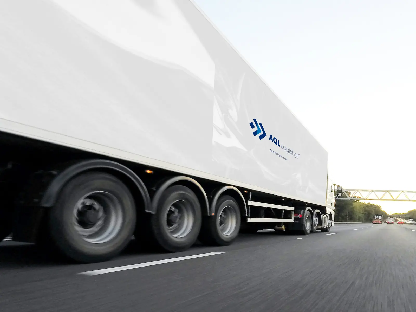 Tractocamión de AQL Logistics con caja refrigerada rotulada circulando en autopista